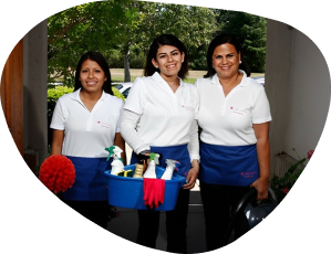 Three women in white shirts and blue aprons holding a basket of cleaning supplies.